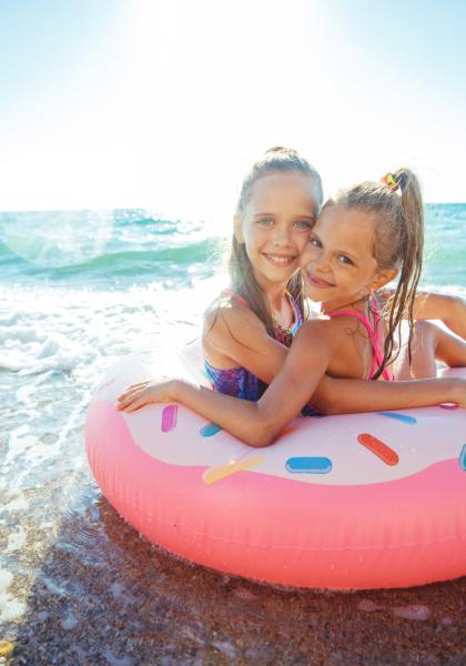 Two smiling girls on an inflatable donut at the beach.