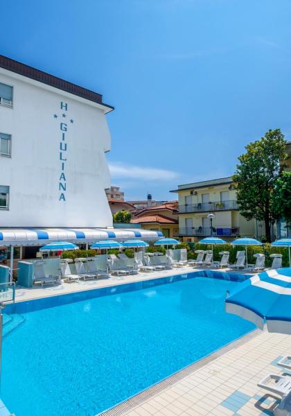 Piscina all'aperto con ombrelloni blu e hotel sullo sfondo.