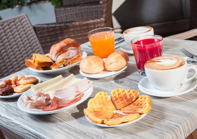 Colazione con caffè, succhi, waffle, pane e affettati.