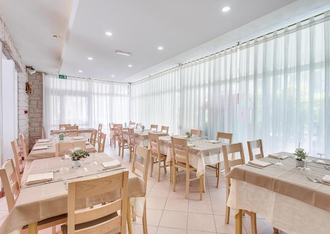 Ristorante luminoso con tavoli apparecchiati e sedie in legno chiaro.