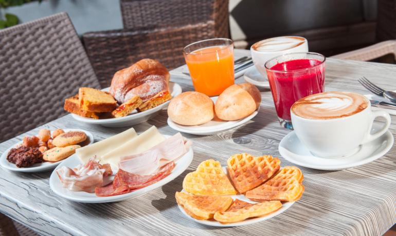 Colazione con caffè, succhi, waffle, pane e affettati.