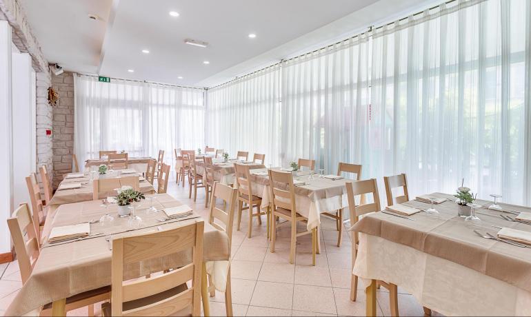 Ristorante luminoso con tavoli apparecchiati e sedie in legno chiaro.