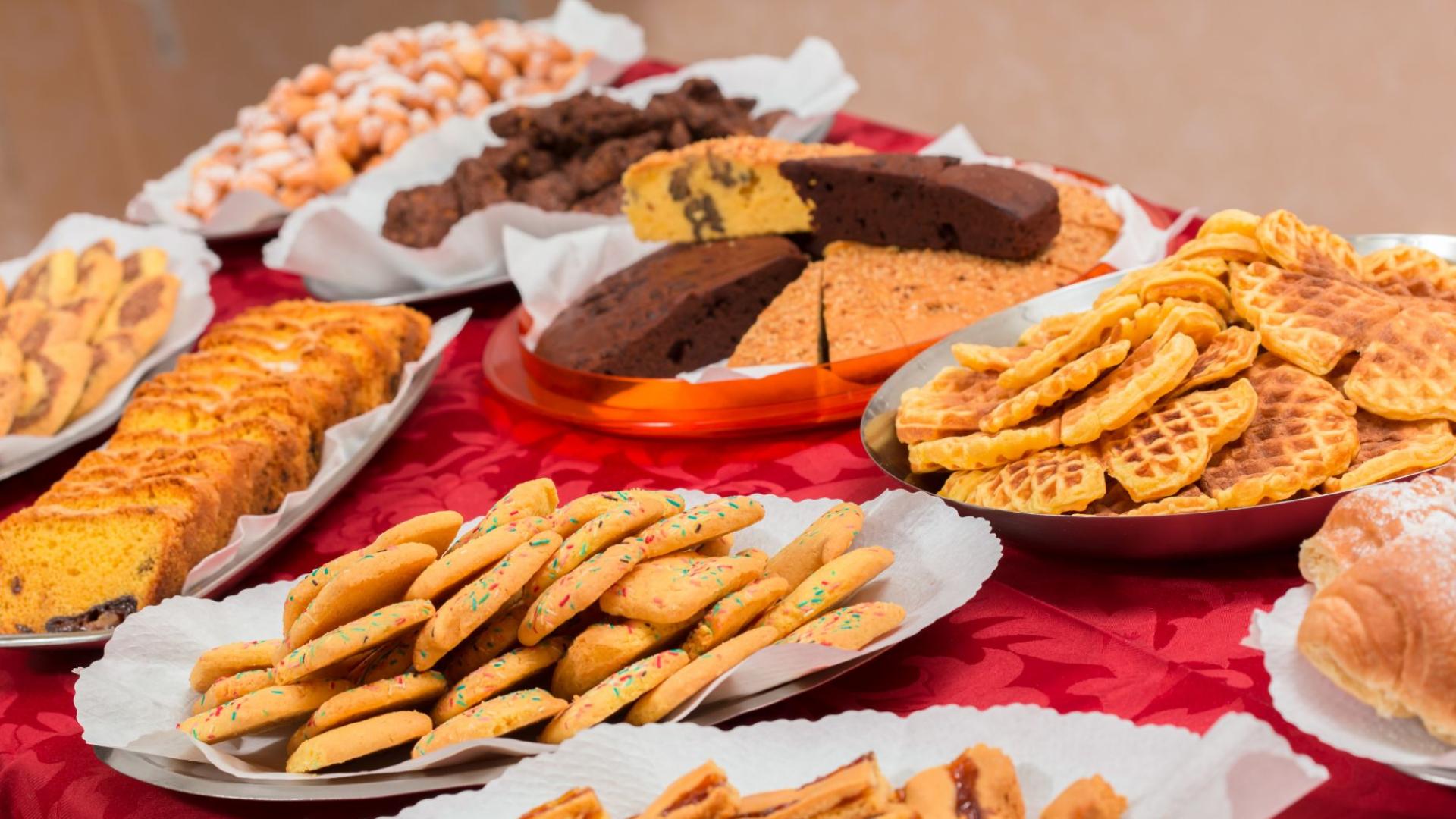 Varietà di dolci su un tavolo rosso, tra cui biscotti e torte.