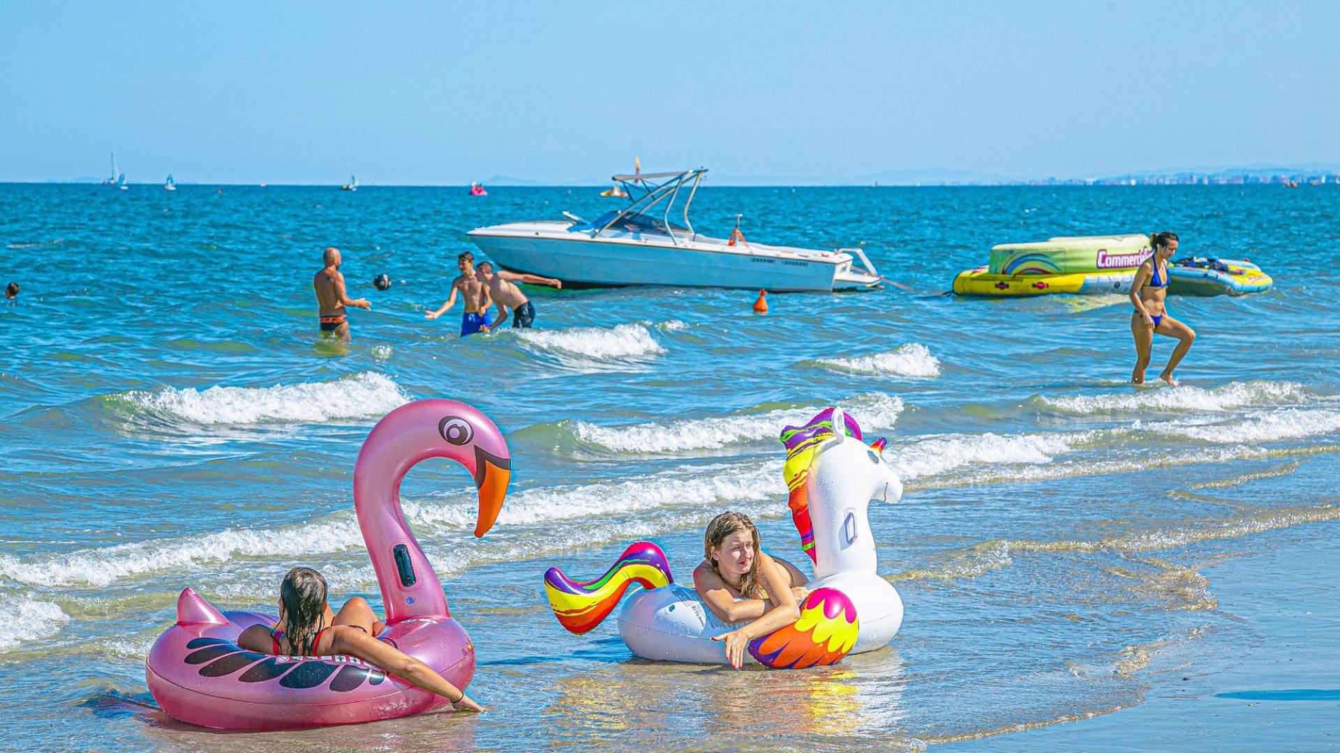 Persone in spiaggia con gonfiabili colorati e barche sullo sfondo.