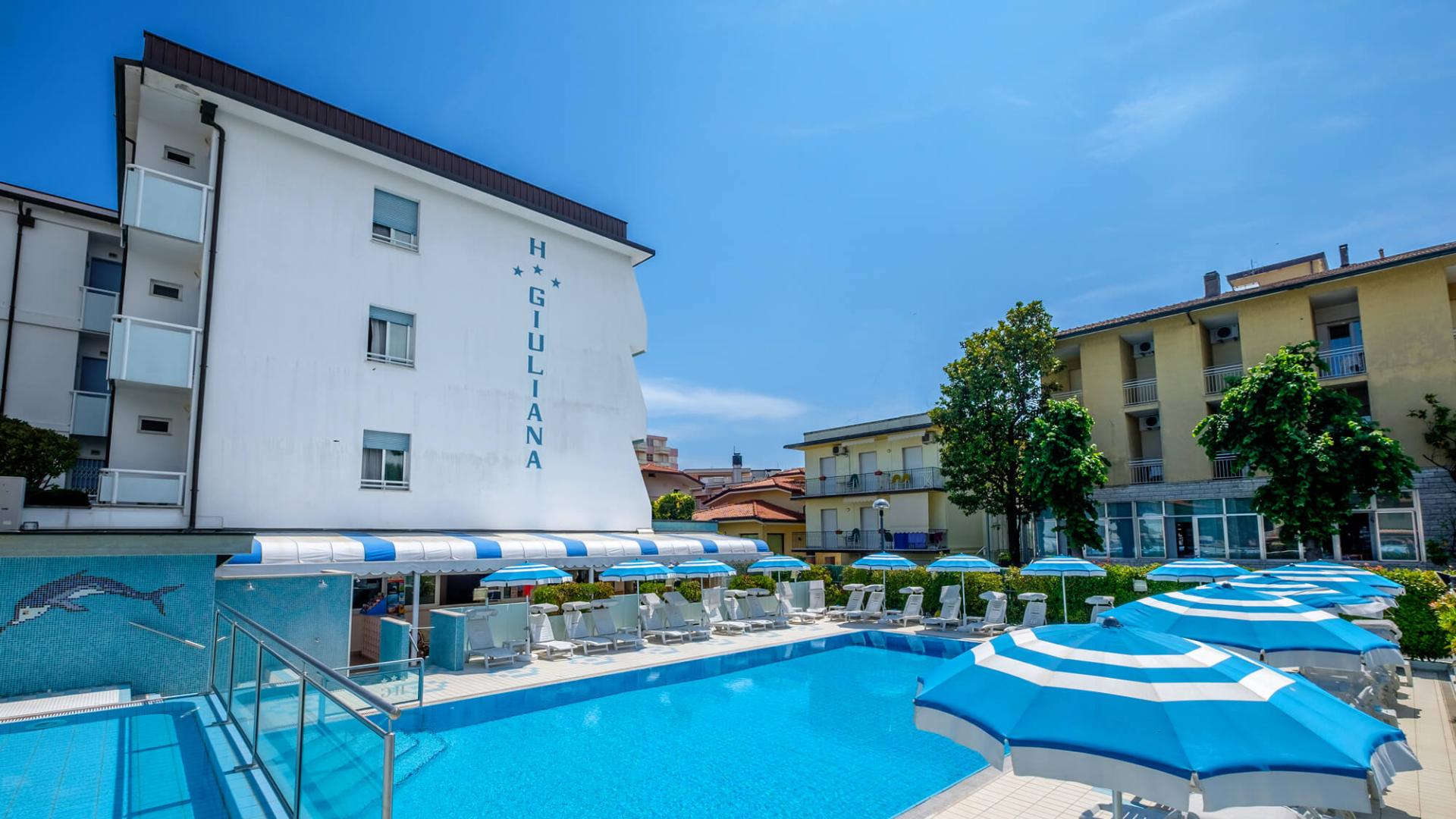 Hotel with a pool and blue umbrellas under a clear sky.