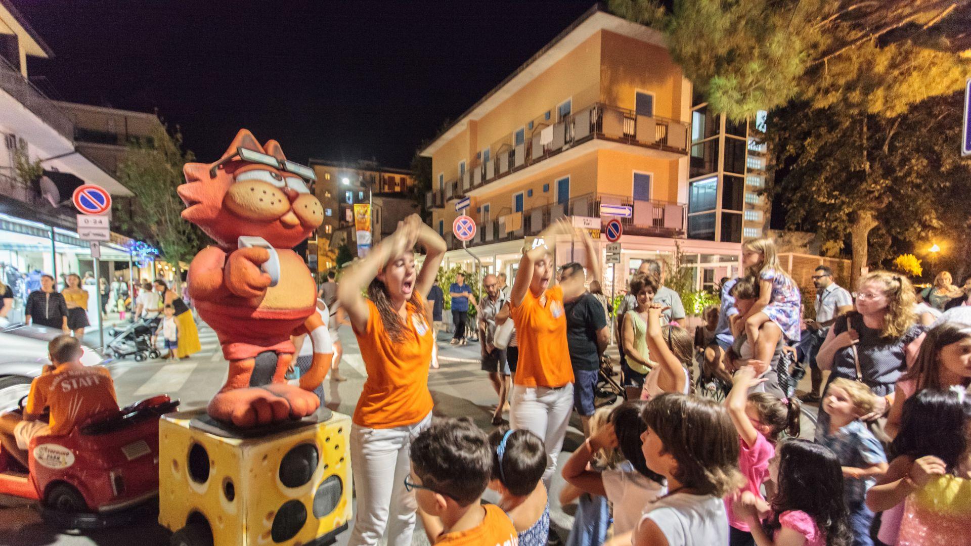 Festa di strada con animatori e statua di gatto.