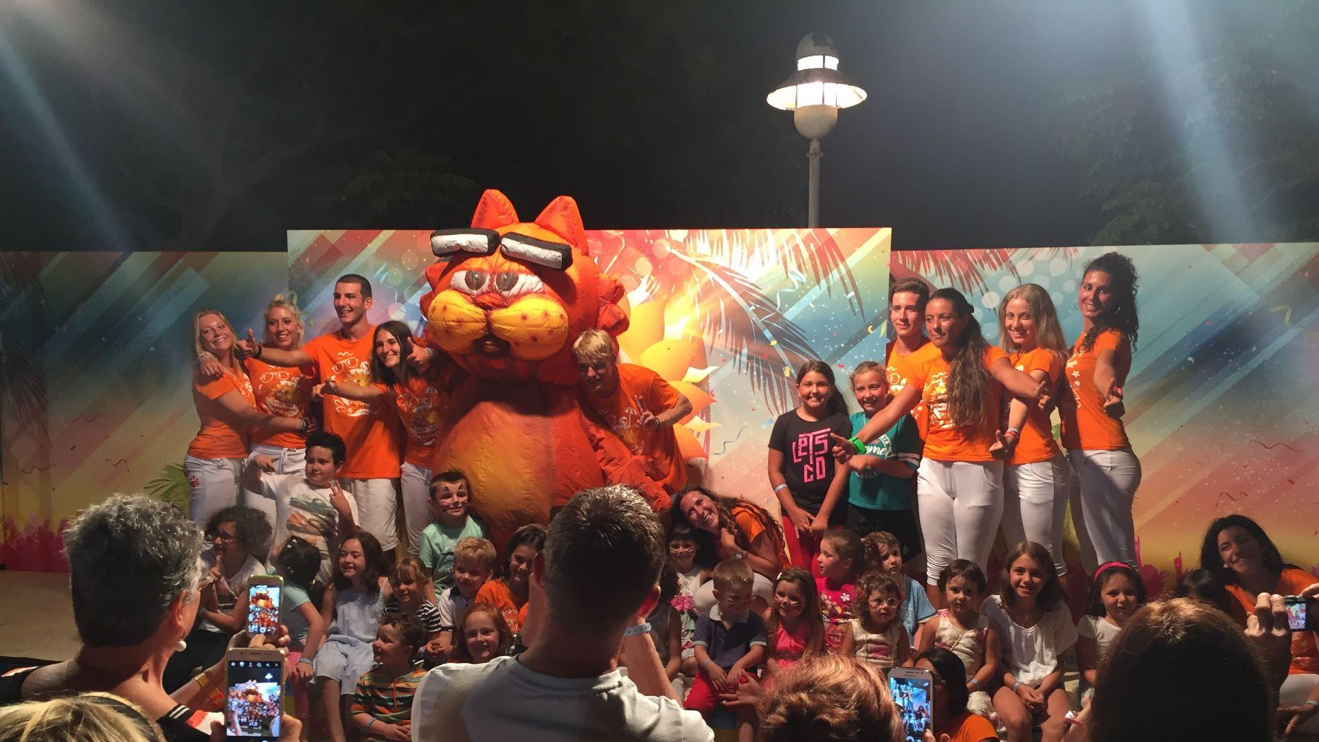 Photo de groupe avec mascotte, adultes et enfants souriants.