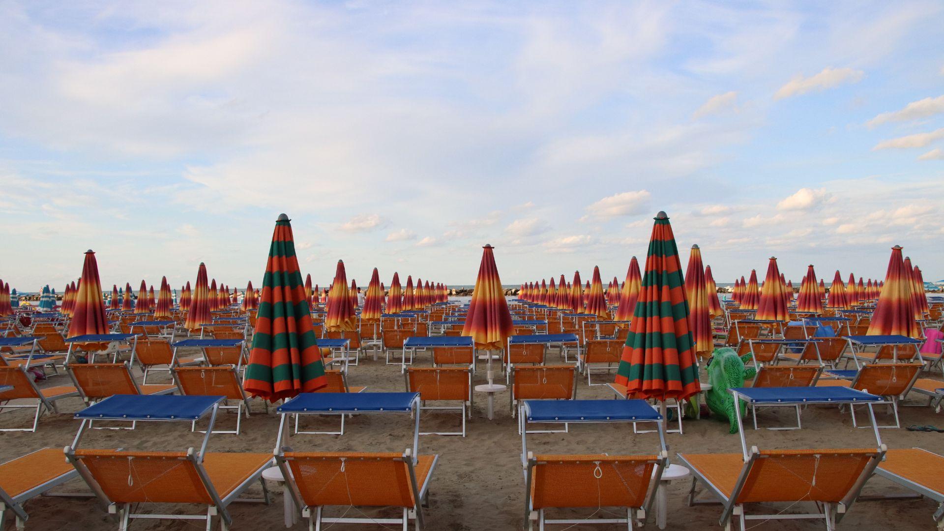 Spiaggia con ombrelloni colorati e lettini vuoti.