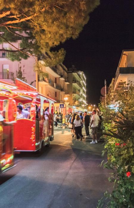 Trenino rosso attraversa la vivace strada notturna.