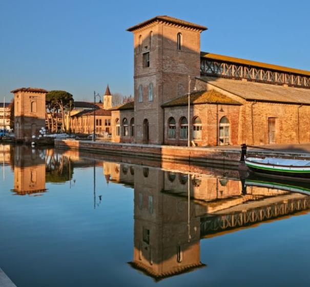 Edificio storico riflesso nell'acqua con barca, cielo sereno.