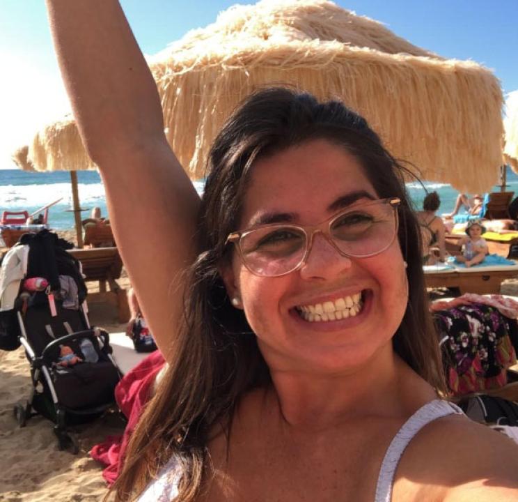 Smiling woman on beach with glasses and straw umbrellas.