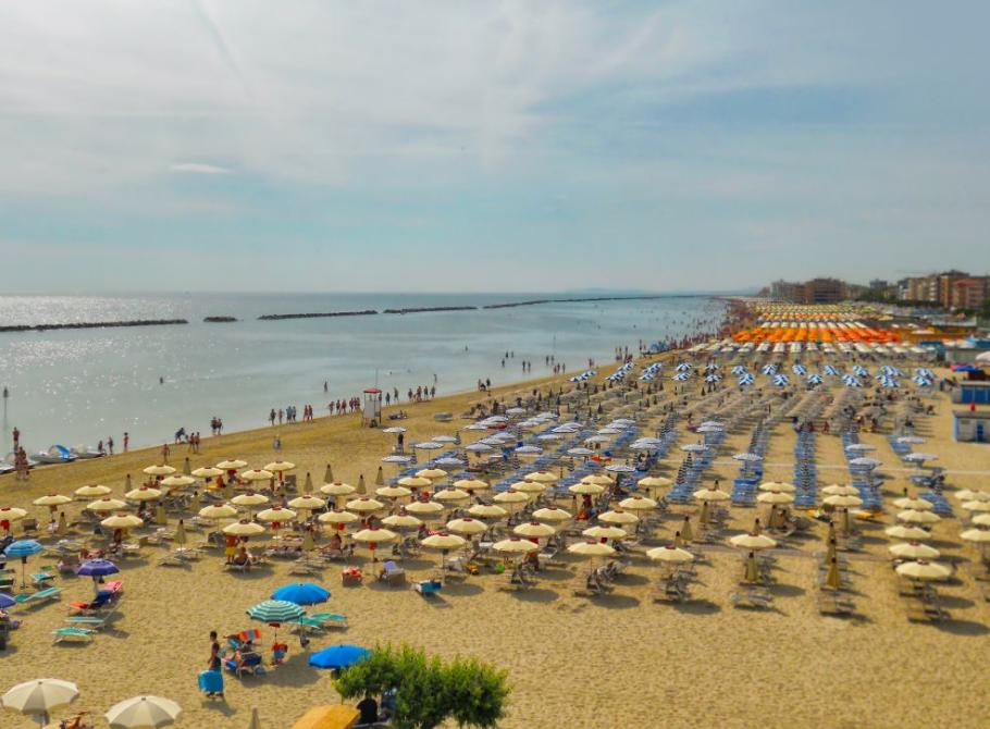 Crowded beach with colorful umbrellas and calm sea.