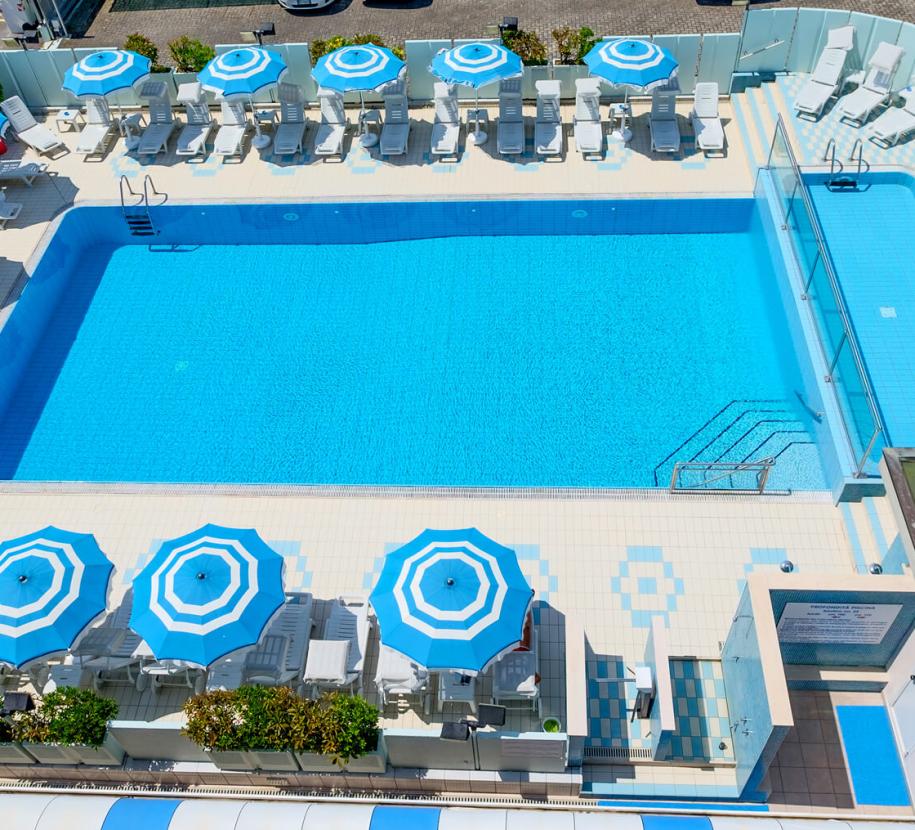 Pool with blue and white umbrellas, loungers, and relaxation area.