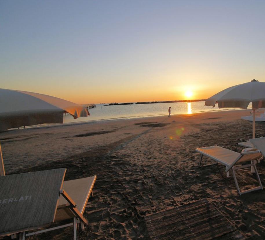 Spiaggia al tramonto con ombrelloni e lettini.